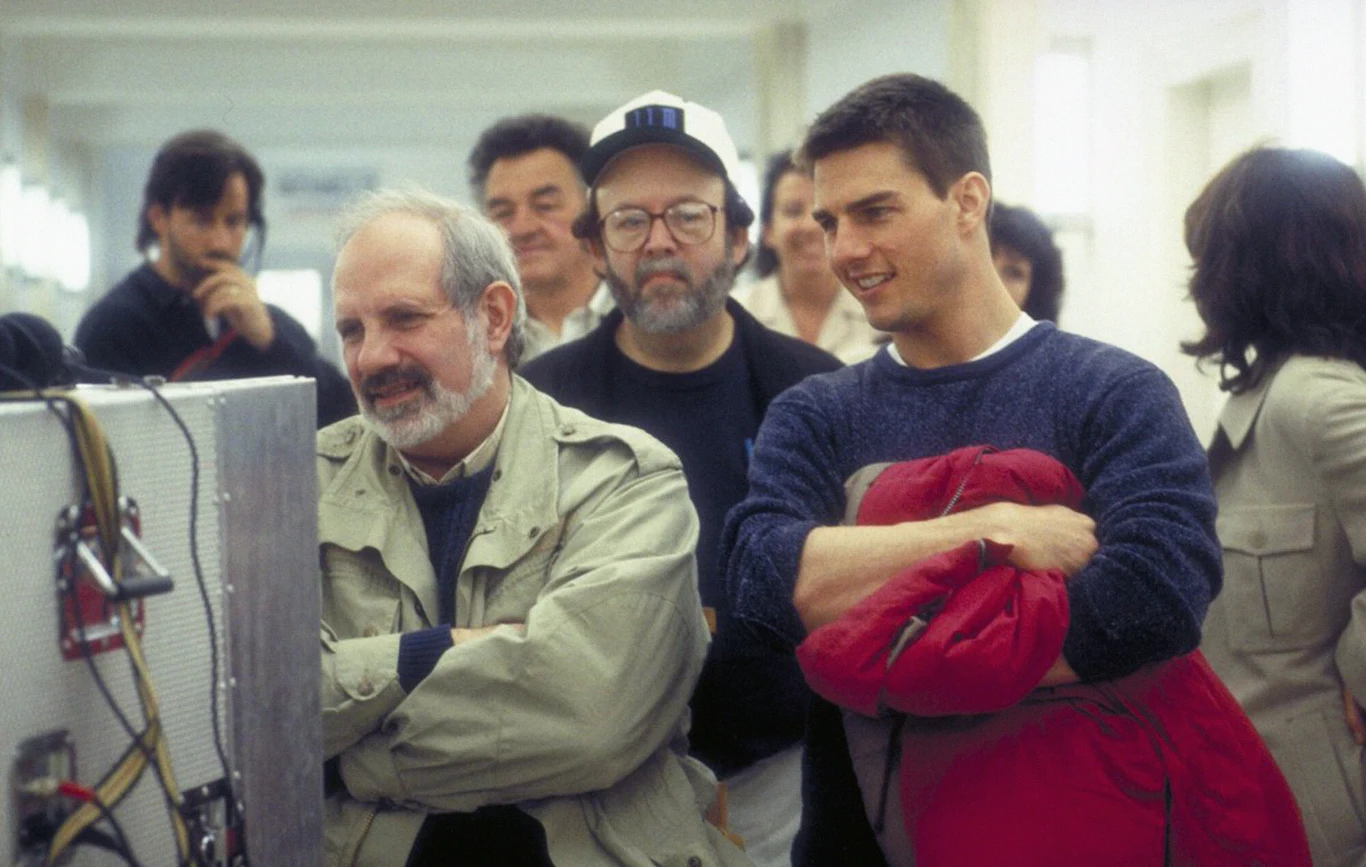 Brian De Palma i Tom Cruise na planie filmu "Mission: Impossible" Grupa mężczyzn skupiona wokół monitora na planie filmowym, wśród nich dwie osoby stojące najbliżej ekranu z wyrazami zainteresowania na twarzach, jeden trzyma czerwoną kurtkę.