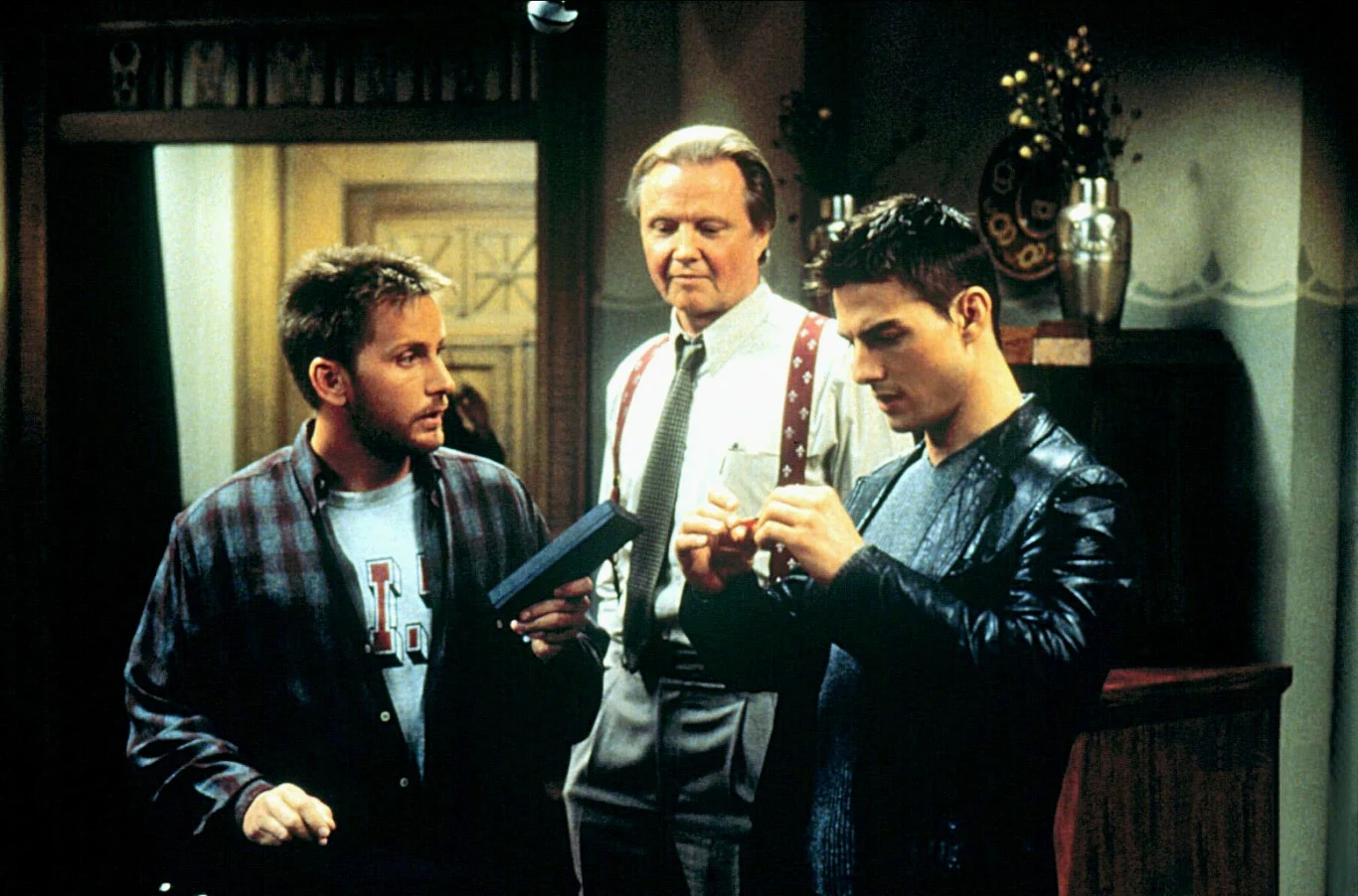 Emilio Estevez, Tom Cruise i Jon Voight w filmie "Mission: Impossible" Trzech mężczyzn skupionych wokół małego przedmiotu, który jeden z nich ogląda z zainteresowaniem, podczas gdy pozostali dwaj przyglądają się z uwagą.