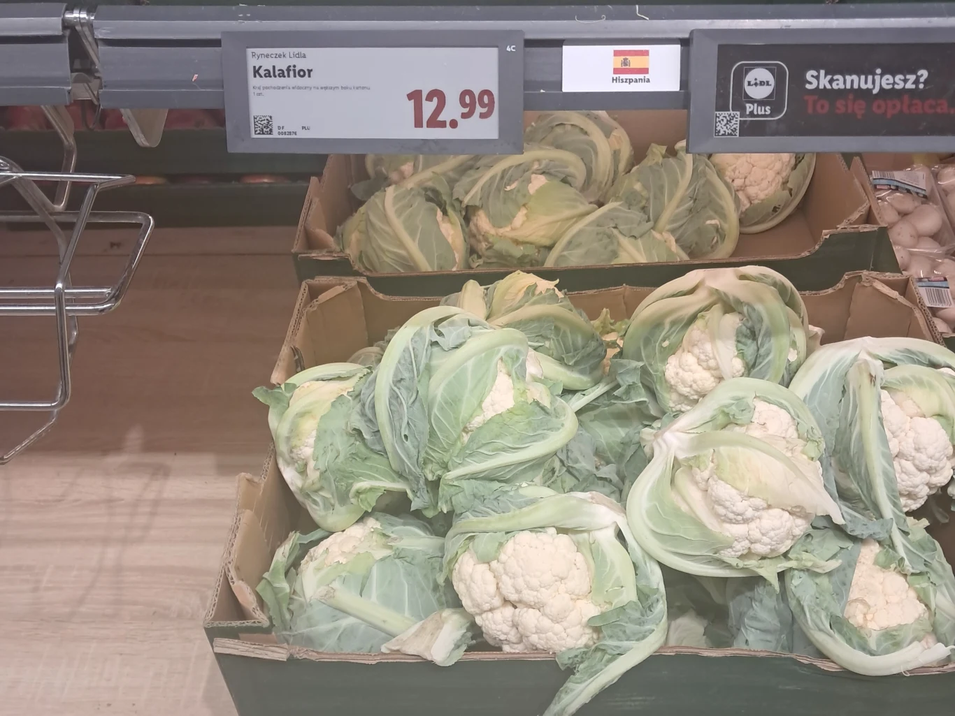 Kilka główek kalafiora ułożonych w kartonowych pudełkach na stoisku warzywnym, cena widoczna na etykiecie powyżej.