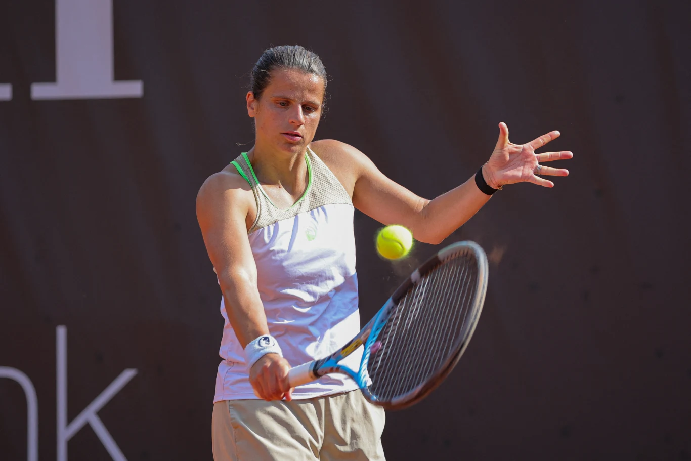 Kobieta w sportowym stroju wykonuje forehand podczas meczu tenisowego, skupiona na odbiciu zbliżającej się piłki.