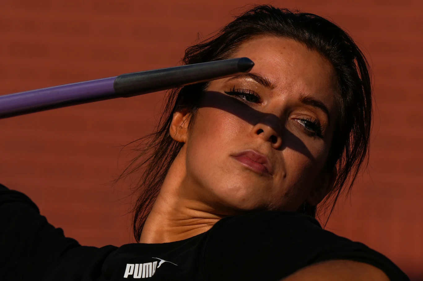 Maria Andrejczyk Kobieta w sportowej koszulce marki Puma koncentruje się podczas rzutu oszczepem, cień pada na jej twarz, podkreślając intensywność momentu.