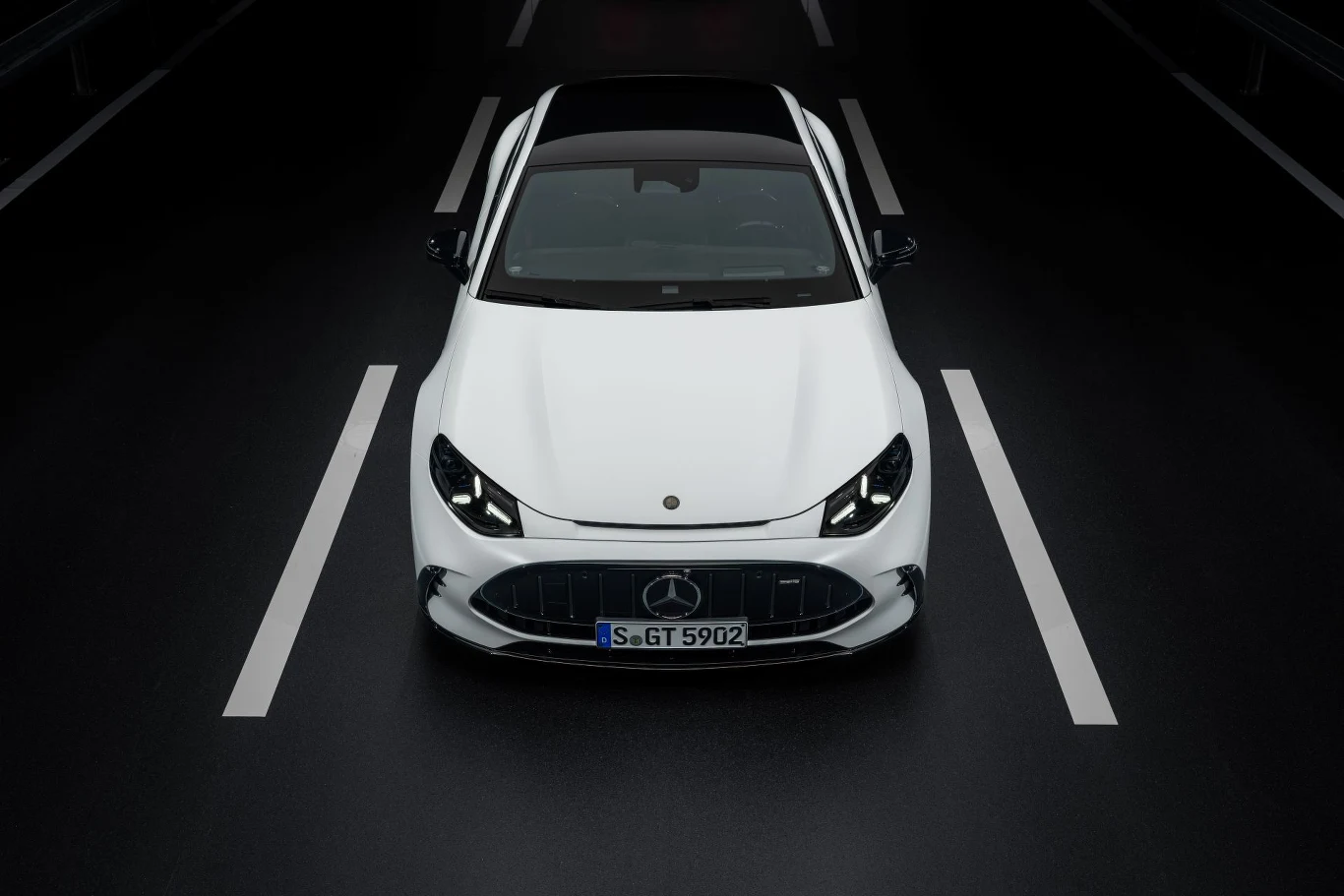Biały samochód marki Mercedes stojący na środku ciemnej dwupasmowej drogi, widoczny z góry, z wyróżniającym się czarnym dachem i charakterystycznym przednim grillem.
