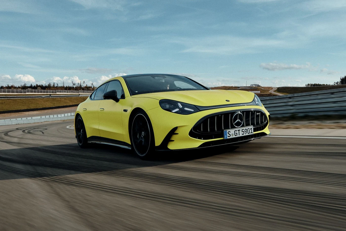 Jaskrawożółty sportowy Mercedes z charakterystycznym grillem i czarnymi detalami dynamicznie pokonuje zakręt na torze wyścigowym.