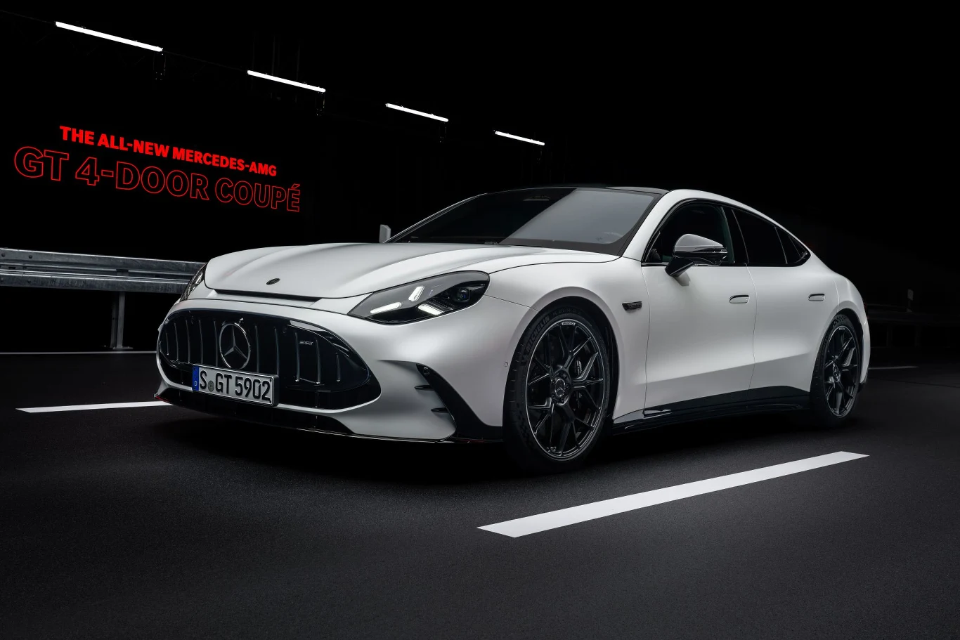 Biały Mercedes-AMG GT 4-Door Coupé w nowoczesnej stylistyce, z charakterystycznym sportowym grillem, czarnymi felgami i dynamiczną sylwetką oświetloną w minimalistycznej, miejskiej scenerii.