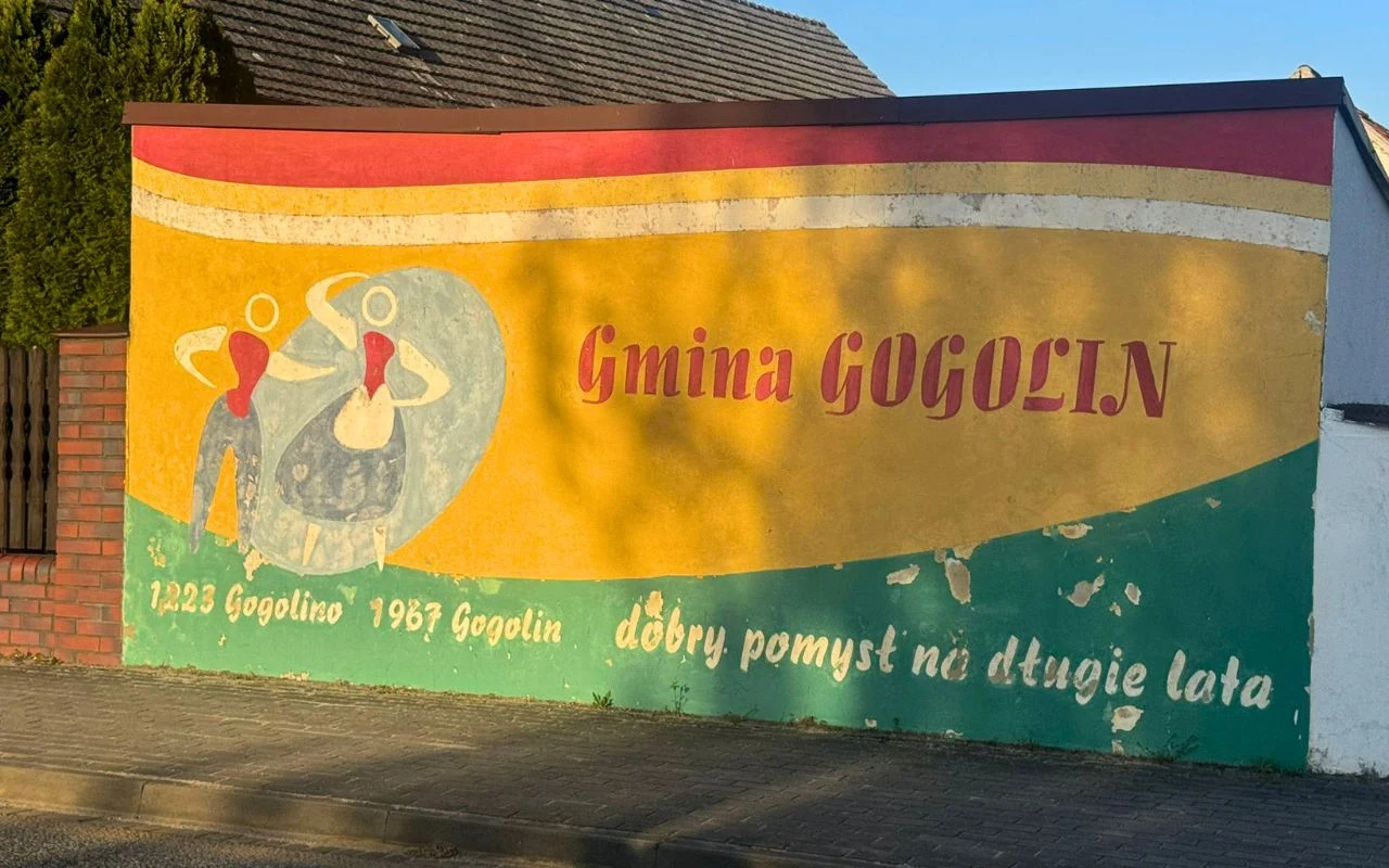 Kolorowy mural z napisem „Gmina Gogolin”, sylwetkami dwóch tańczących osób w strojach ludowych oraz hasłem „dobry pomysł na długie lata” i datami 1223 Gogolino oraz 1967 Gogolin.