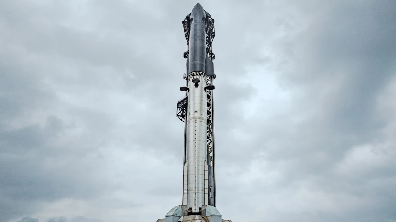 Pionowo stojąca rakieta kosmiczna o metalicznej powierzchni, przygotowana do startu na tle pochmurnego nieba.