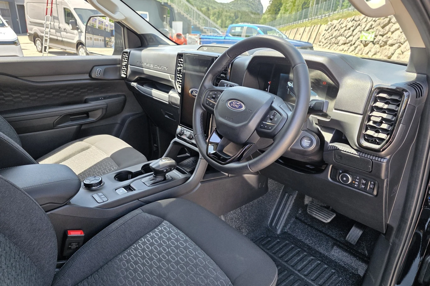 Wnętrze nowoczesnego samochodu marki Ford z widoczną kierownicą, panelem sterowania, automatyczną skrzynią biegów oraz dwoma ekranami na desce rozdzielczej.
