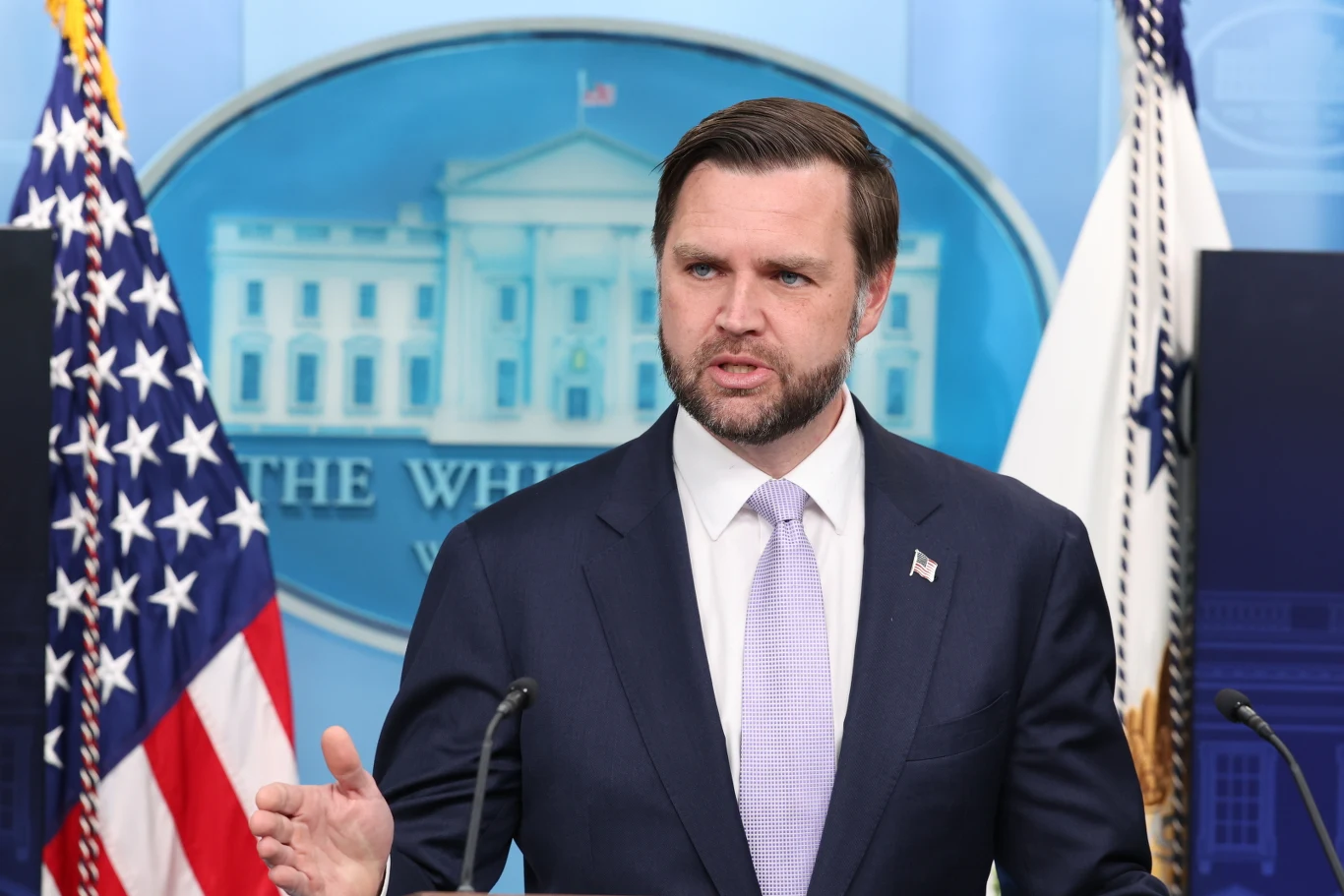 Wiceprezydent USA J.D. Vance o zamieszaniu ws. niewysłania amerykańskich żołnierzy do Polski J.D. Vance przy mównicy z mikrofonem, gestykuluje na tle flagi USA i wizerunku Białego Domu.