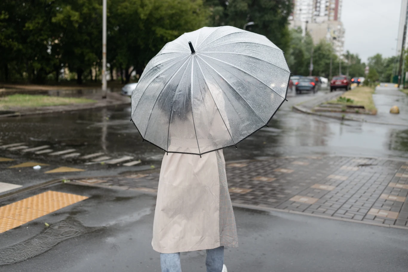 W najbliższych dniach w wielu regionach kraju pojawią się opady deszczu, ale w przyszłym tygodniu zrobi się bardzo ciepło Osoba w jasnym płaszczu przeciwdeszczowym z przezroczystym parasolem idzie po mokrym chodniku w mieście podczas deszczu