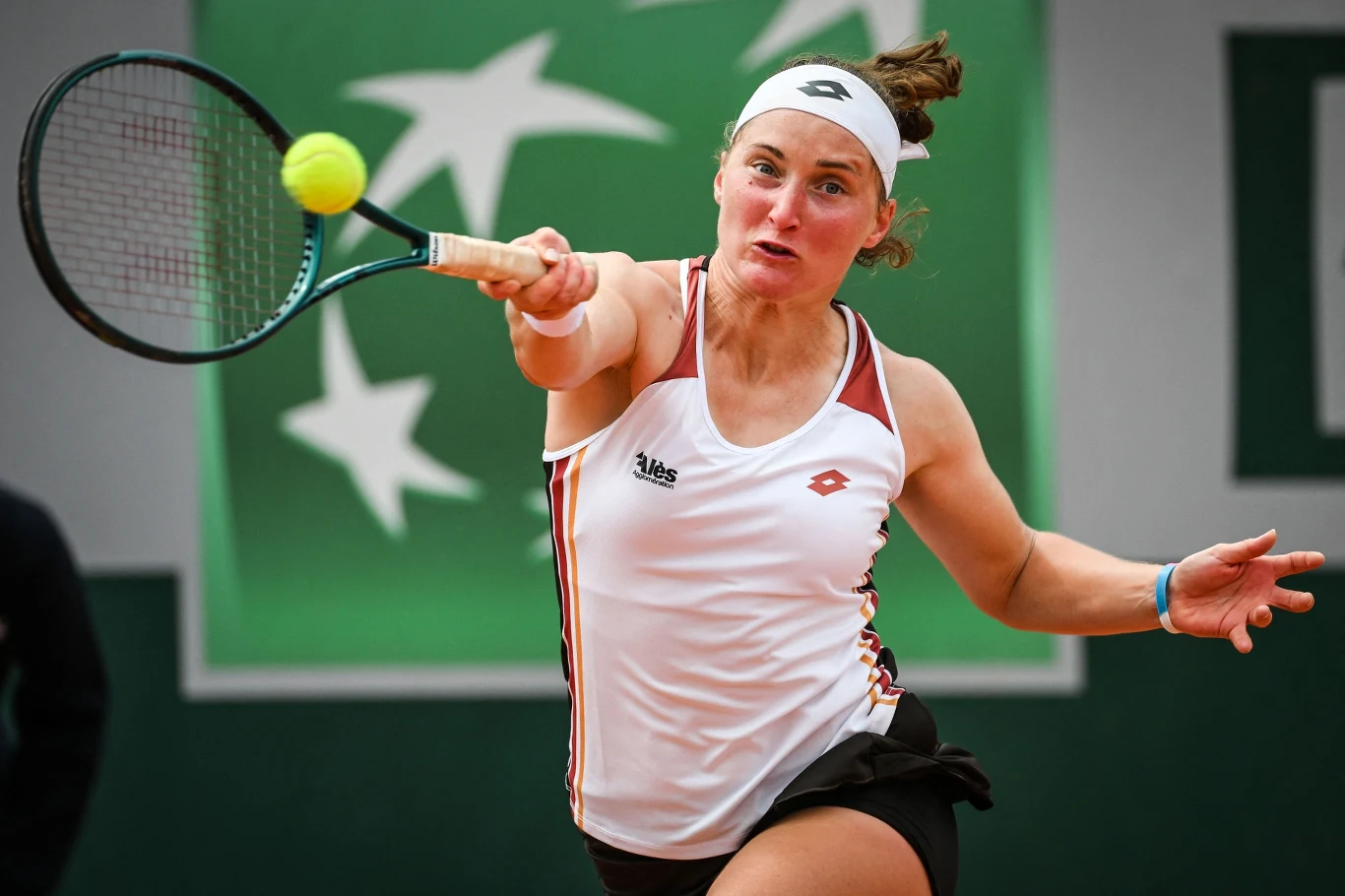 Carole Monnet Tenista con traje blanco durante un golpe de raqueta dinámico, centrándose en una pelota de tenis amarilla.