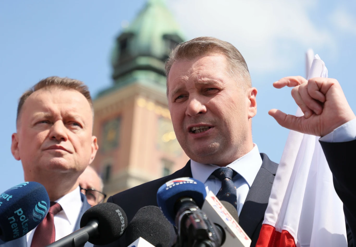 Przemysław Czarnek przemawiał przed rozpoczęciem manifestacji organizowanej przez NSZZ "Solidarność" Przemysław Czarnek przemawia przed mikrofonami, przy polskiej fladze, w tle wieża z zieloną kopułą.
