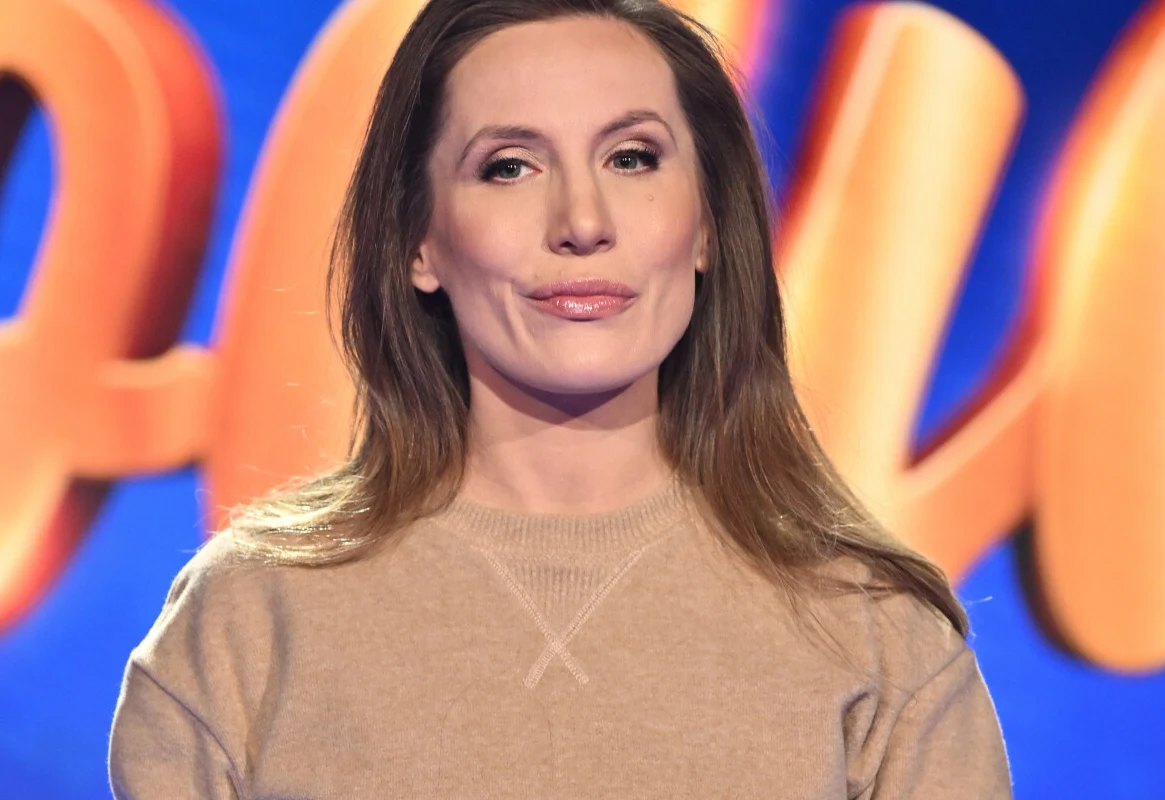 Pola Wiśniewska Pola Wiśniewska z długimi brązowymi włosami, ubrana w beżowy sweter, na tle kolorowej grafiki.
