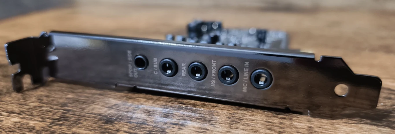 Metalowy panel z pięcioma gniazdami audio typu jack, każde oznaczone inną funkcją, zamontowany na tle drewnianej powierzchni.