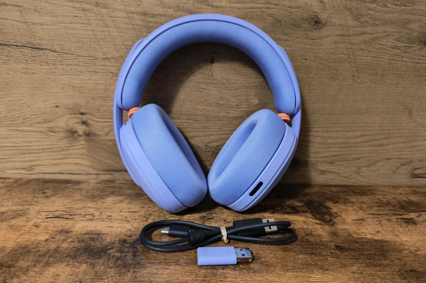 Bezprzewodowe słuchawki nauszne w kolorze fioletowym, przed którymi leżą przewód USB oraz adapter USB do połączenia bezprzewodowego.
