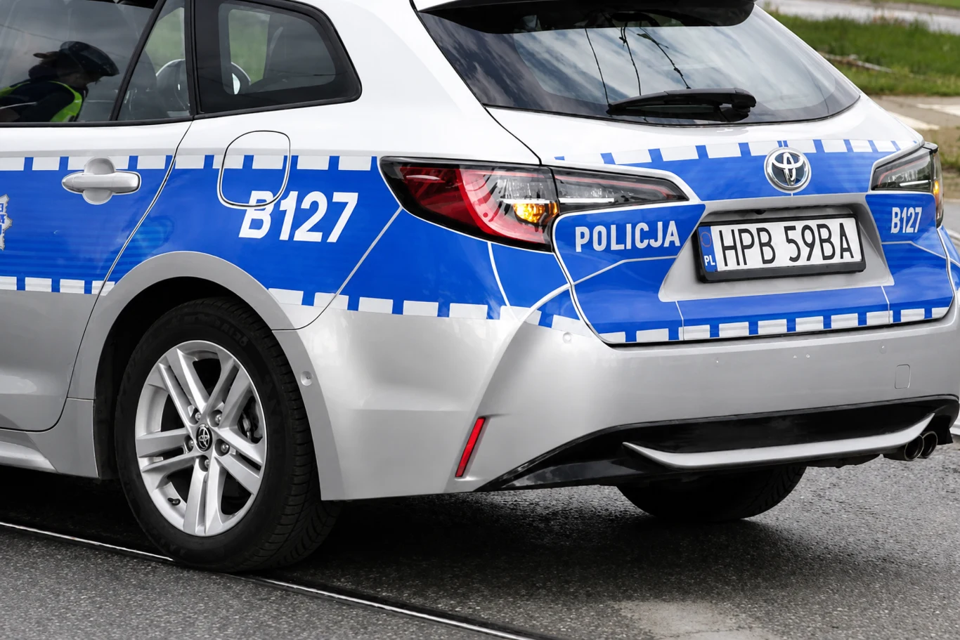 Co oznacza ciąg cyfr i liter na radiowozie policyjnym? Tył oznakowanego radiowozu polskiej policji z niebiesko-białym oznaczeniem, numerem bocznym B127 i tablicą HPB 59BA