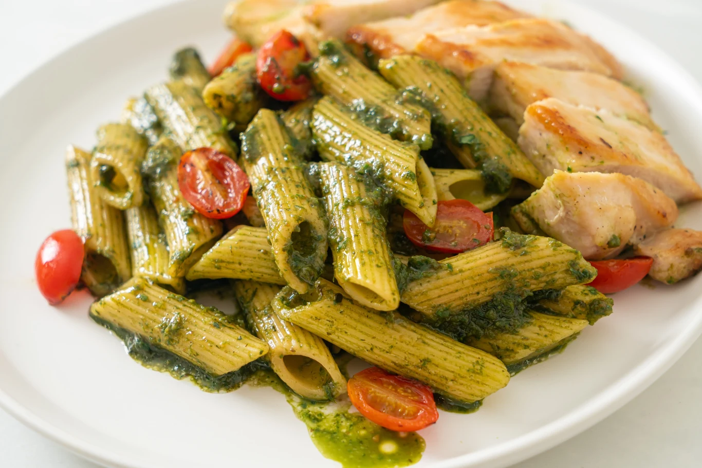 Makaron penne z sosem pesto i świeżymi pomidorkami koktajlowymi, podany z grillowanym filetem z kurczaka.