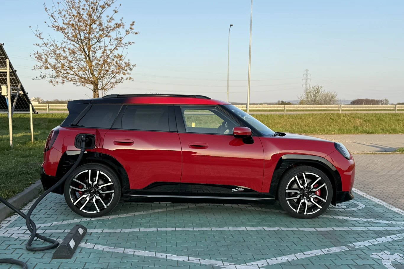 Czerwony samochód elektryczny typu SUV podłączony do stacji ładowania na wyznaczonym miejscu parkingowym.