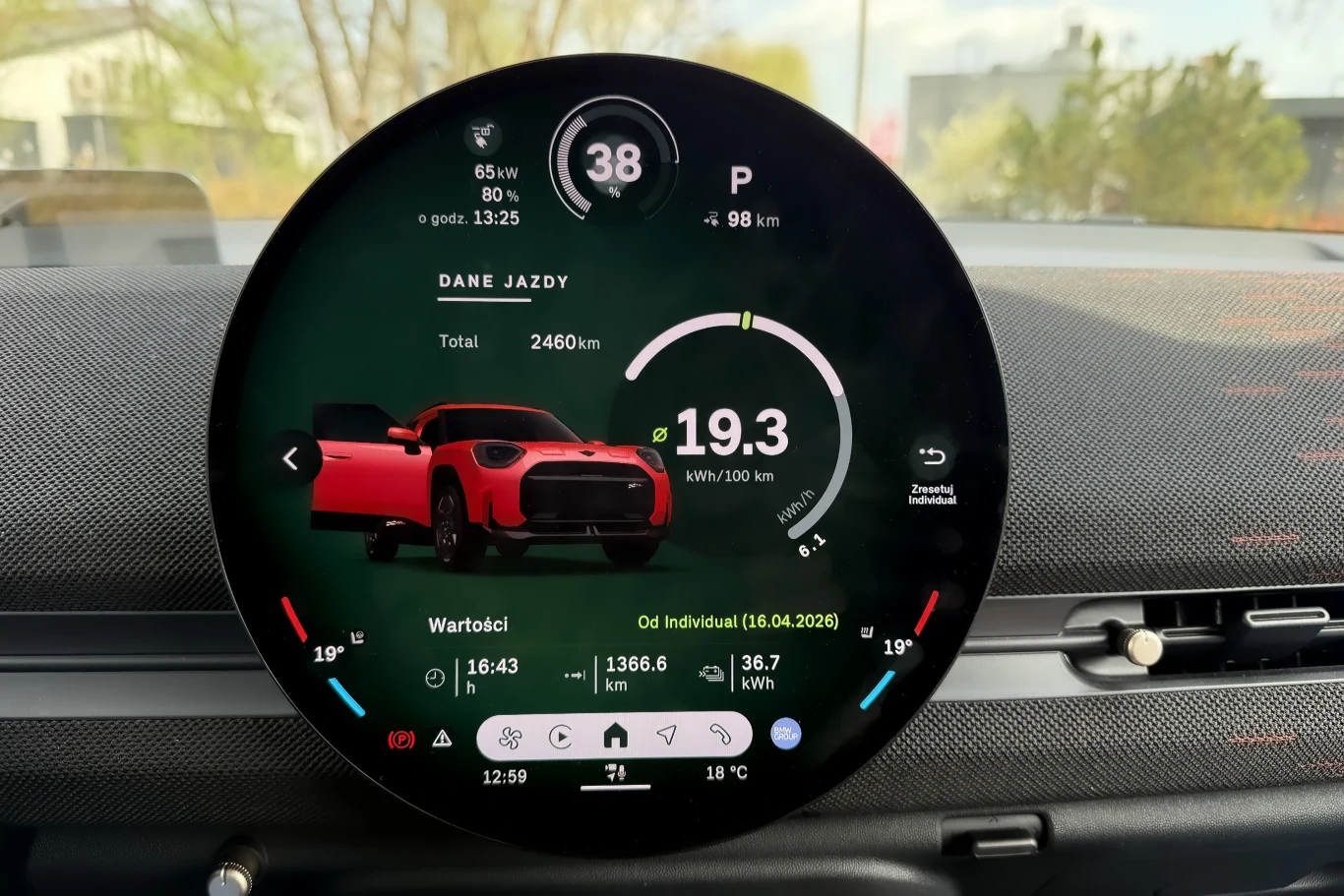 Okrągły ekran komputera pokładowego wyświetlający podsumowanie jazdy, zużycie energii na poziomie 19,3 kWh/100 km, dystans 2460 km, graficzną prezentację samochodu w kolorze czerwonym oraz szczegółowe dane dotyczące zasięgu i stylu jazdy.