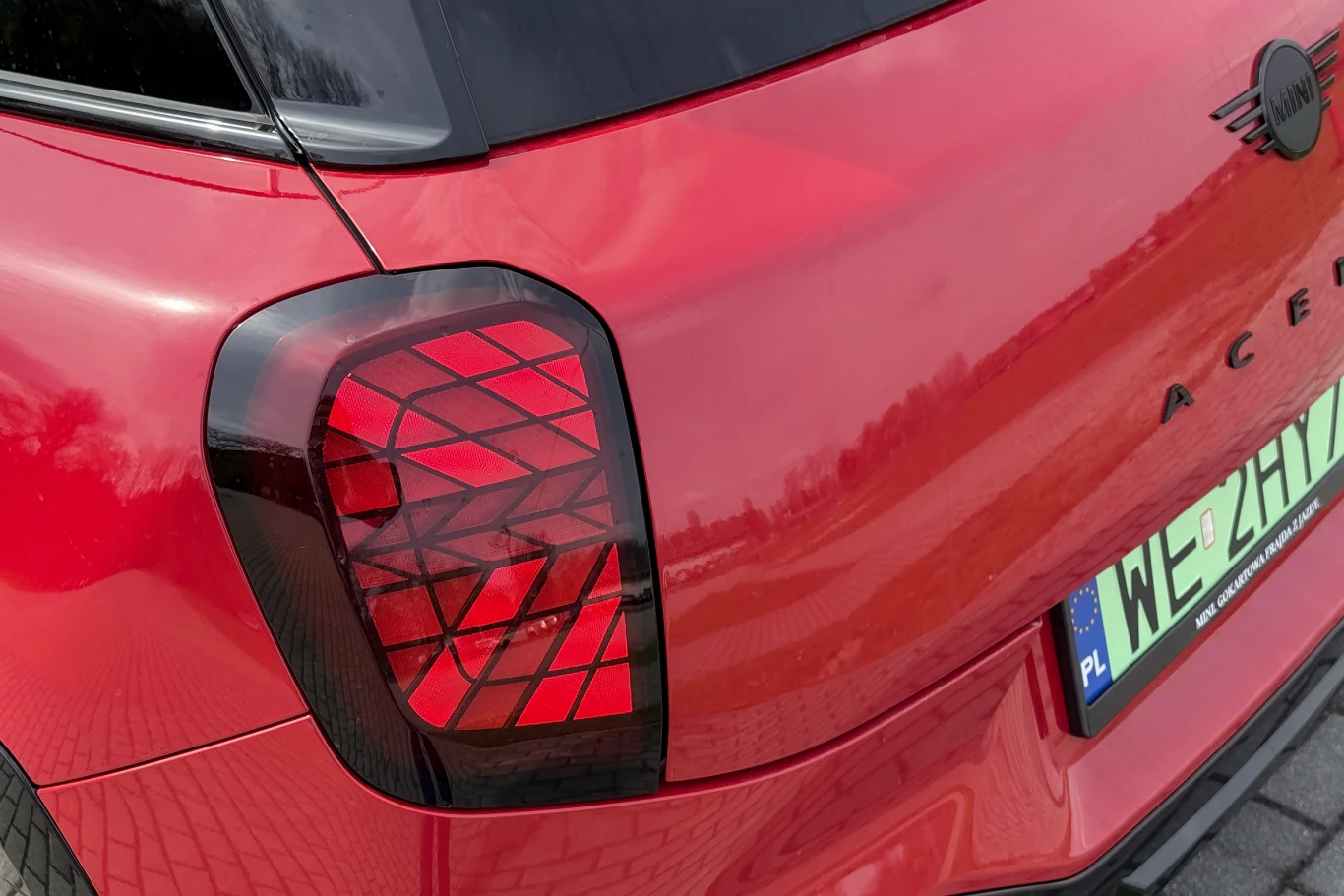 Tylna lampa samochodu MINI o charakterystycznym, geometrycznym wzorze świateł oraz zielona tablica rejestracyjna typu EV z polskim oznaczeniem.