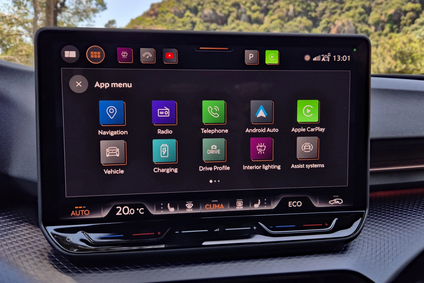 Wyświetlacz systemu multimedialnego samochodu z czytelnie rozmieszczonymi ikonami aplikacji, umożliwiającymi dostęp do nawigacji, radia, telefonu, Android Auto, Apple CarPlay, ustawień pojazdu, ładowania, profilu jazdy, oświetlenia wnętrza oraz systemó...