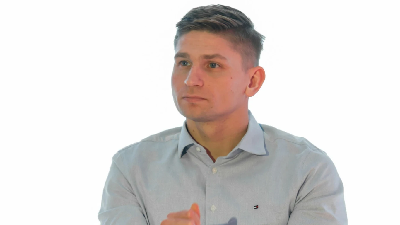 Mężczyzna w jasnoniebieskiej koszuli z krótkimi włosami, skierowany lekko w lewo, z poważnym wyrazem twarzy na jasnym tle.
