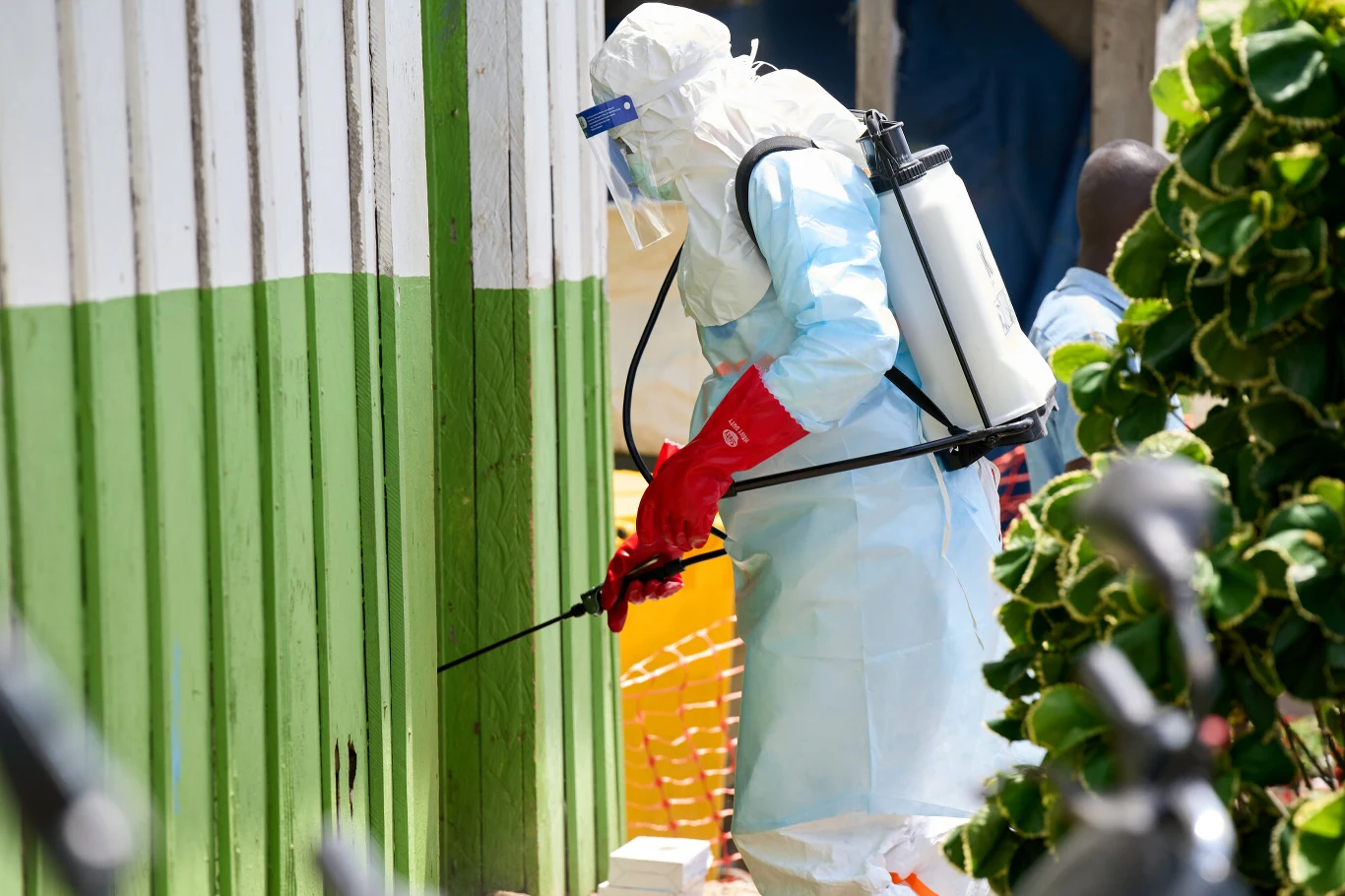 Epidemia Eboli w Demokratycznej Republiki Konga jest pod kontrolą Osoba w pełnym kombinezonie ochronnym, z maską i rękawicami, dezynfekuje ścianę budynku, używając opryskiwacza plecakowego.