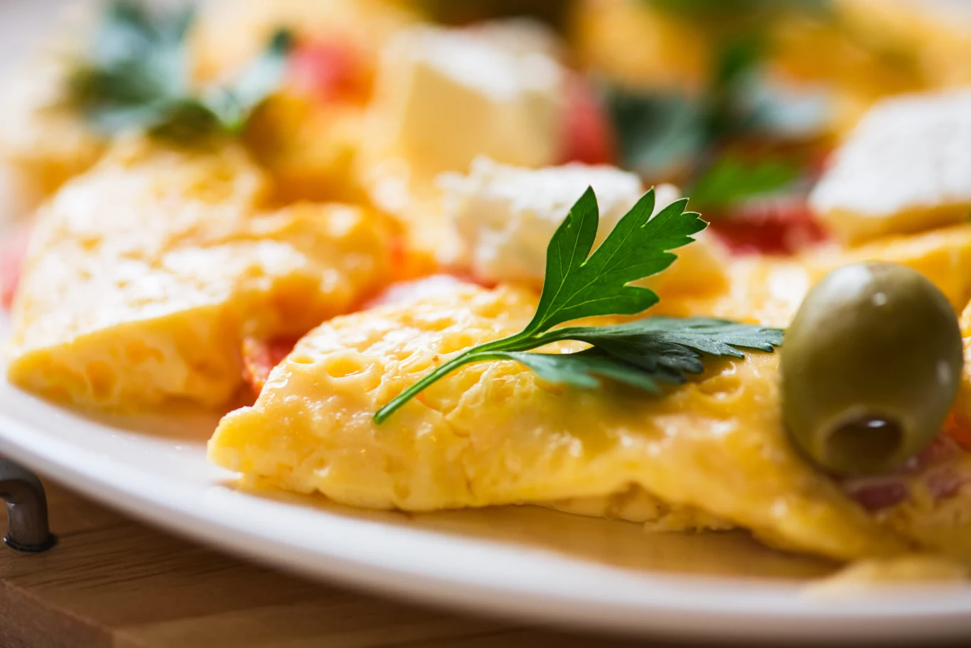 Jak zrobić puszysty omlet? Porcja puszystego omletu z zieloną oliwką, pietruszką i serem feta na białym talerzu.