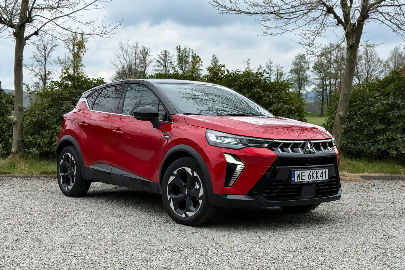 Czerwony, pięciodrzwiowy SUV o nowoczesnym designie nadwozia, masywny przód z LED-owymi reflektorami oraz charakterystycznymi wlotami powietrza, czarne elementy nadwozia kontrastujące z karoserią, czarne felgi, samochód ustawiony na żwirowej nawierzchni.