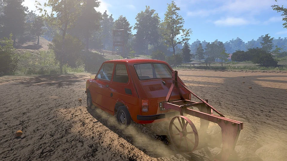 Czerwony fiat 126p z podczepionym pługiem orze piaszczyste pole w słoneczny dzień, w tle las i delikatnie zamglone drzewa.