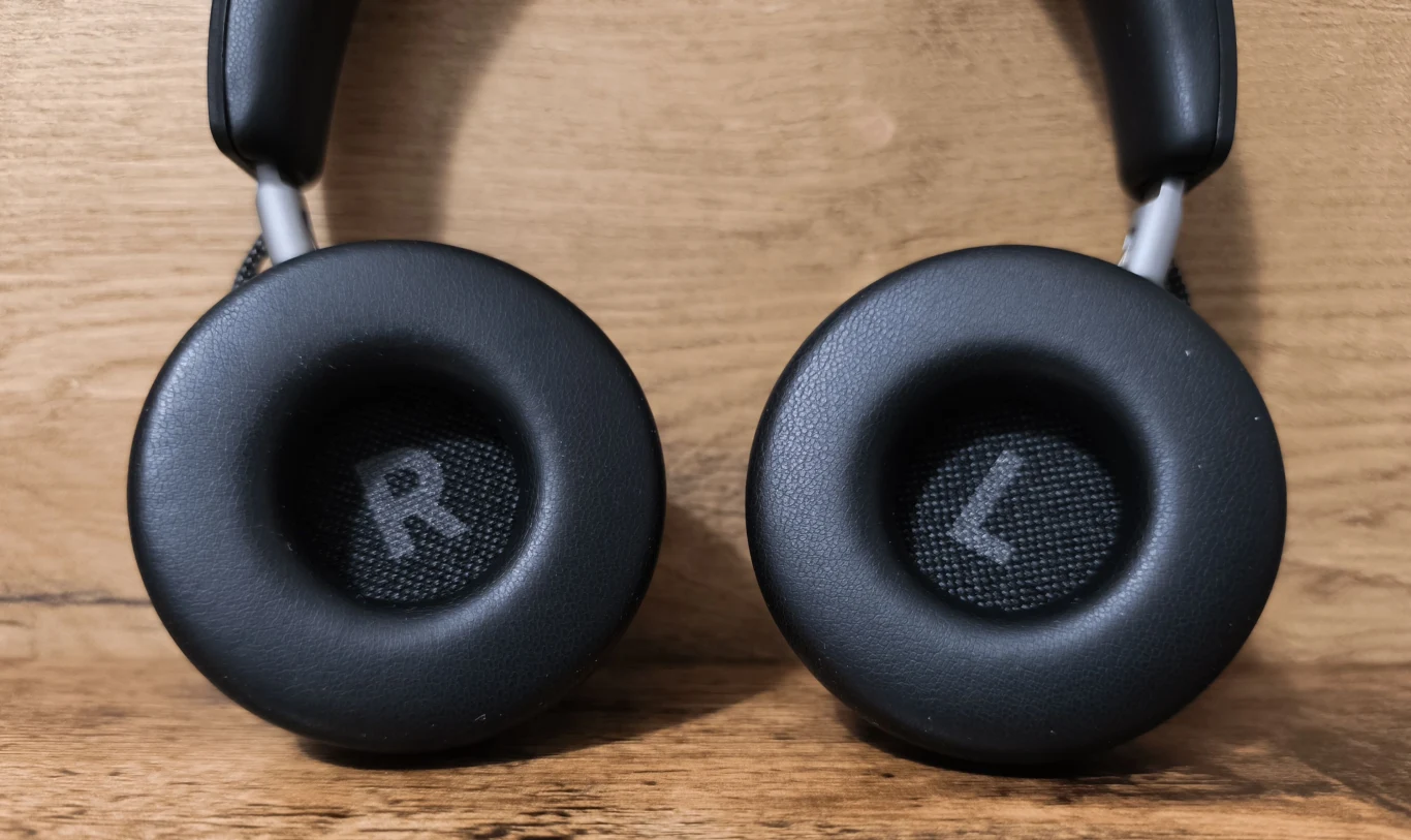 Beyerdynamic Aventho 100 Czarne nauszniki słuchawek z oznaczeniami R i L na środku każdej muszli, ustawione na tle drewnianej powierzchni.