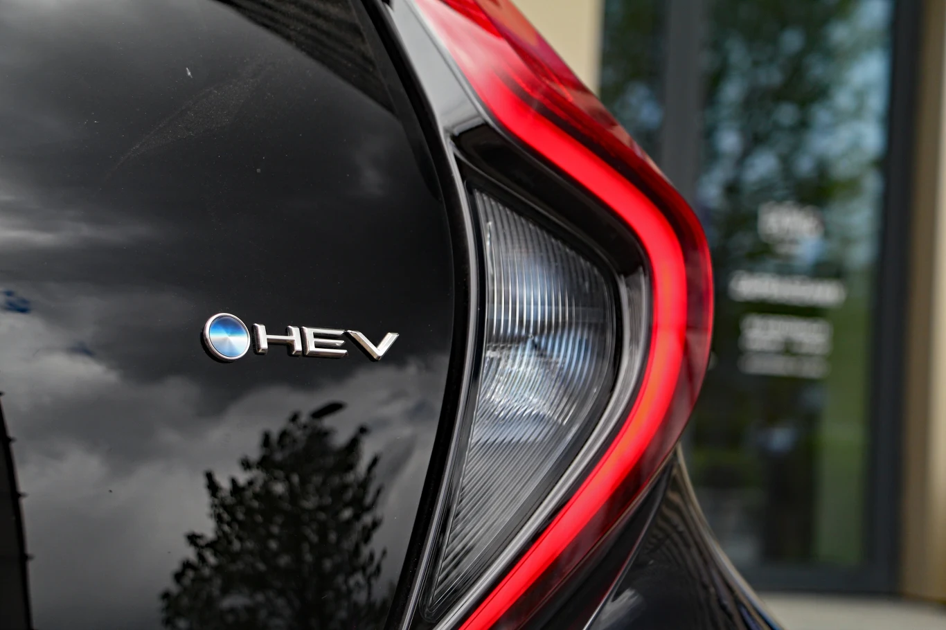 Toyota Aygo X Hybrid Tylny reflektor samochodu oznaczonego emblematem HEV i charakterystycznym czerwonym akcentem świetlnym na czarnym lakierze.