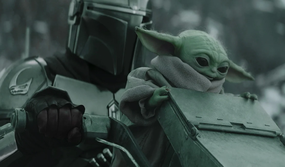 "Gwiezdne wojny: Mandalorian i Grogu" Mandalorianin prowadzi pojazd, obok niego Grogu w płaszczu. Scena z filmu "Gwiezdne wojny: Mandalorian i Grogu".