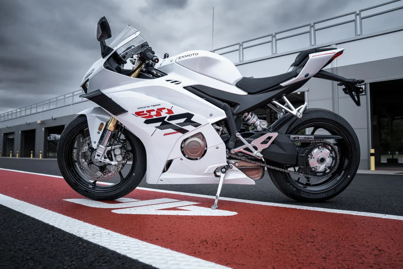 biały sportowy motocykl ustawiony na czerwonym pasie toru wyścigowego, dynamiczna sylwetka i charakterystyczne oznaczenia na bocznej owiewce