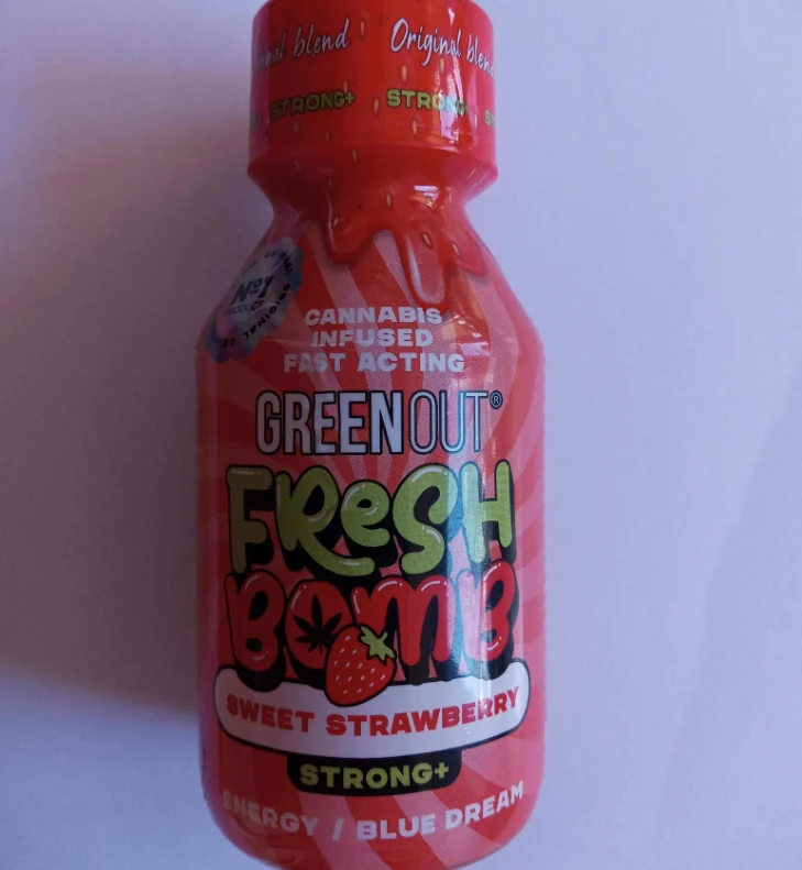 Butelka napoju Green Out Fresh Bomb o smaku słodkiej truskawki, zawierającego ekstrakt z konopi, z wyraźnym oznaczeniem siły działania Strong+, utrzymana w czerwonej kolorystyce z grafiką truskawki.