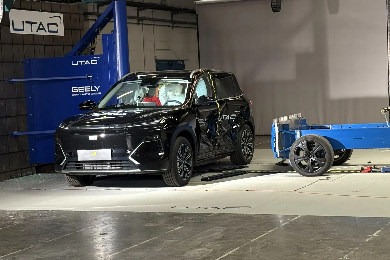 Czarny samochód SUV podczas testu zderzeniowego w zamkniętej hali, obok znajduje się niebieska przesuwna bariera uderzeniowa.