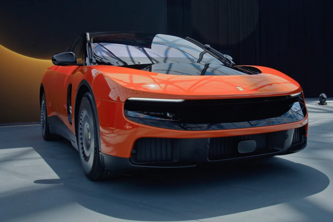Ferrari Luce Nowoczesny, sportowy samochód w jaskrawopomarańczowym kolorze z czarnym dachem, charakterystycznym przednim pasem i aerodynamicznymi liniami nadwozia.
