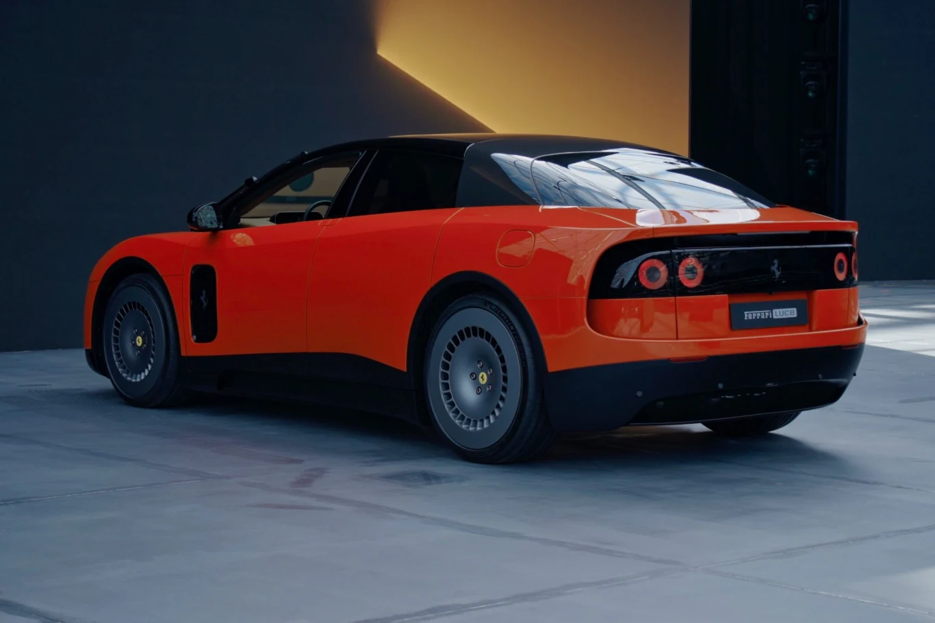Sportowy samochód Ferrari w intensywnie pomarańczowym kolorze z czarnym dachem, nowoczesnymi tylnymi światłami i charakterystycznymi felgami, ustawiony na betonowej powierzchni w minimalistycznym otoczeniu.