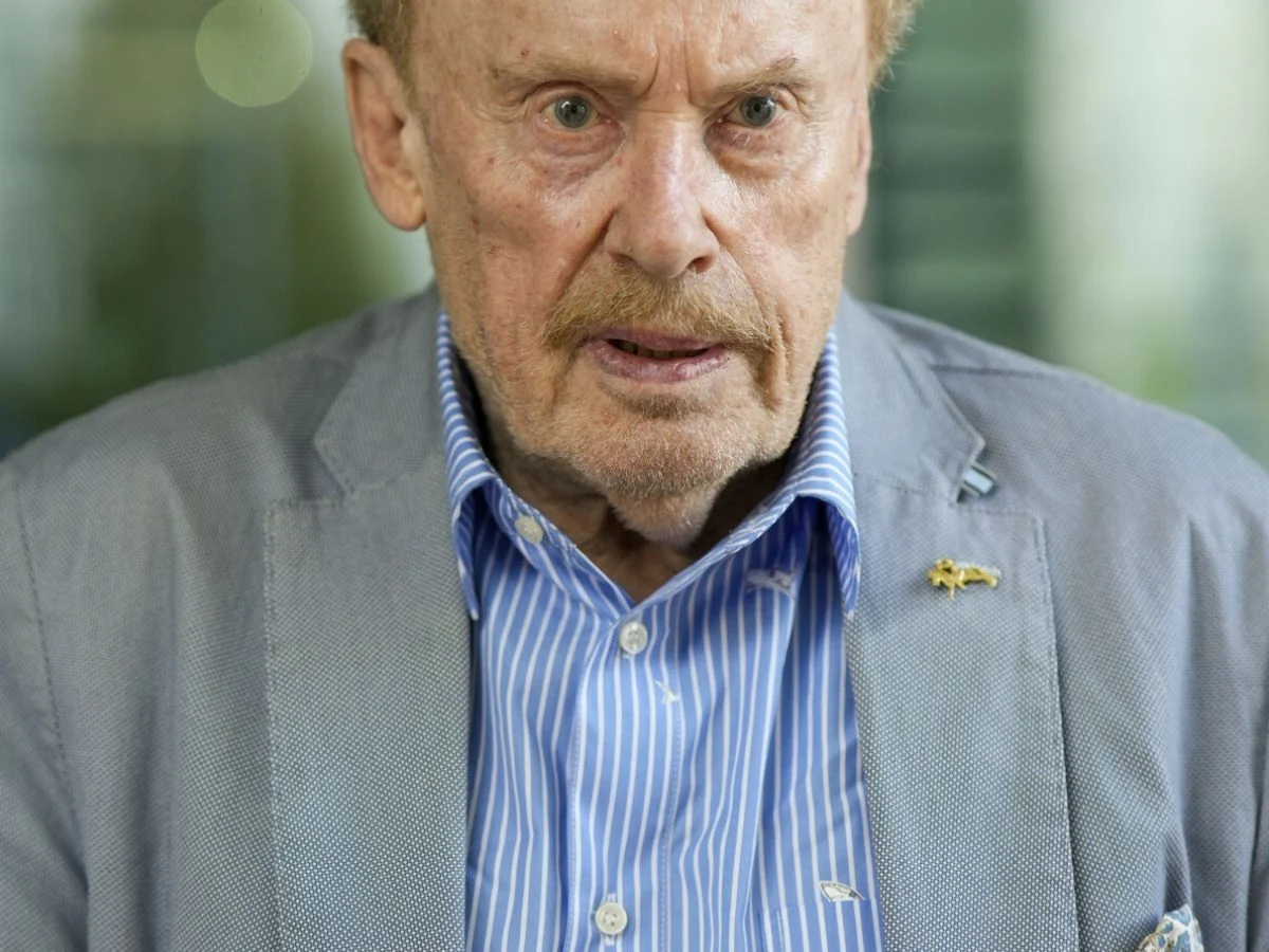 Daniel Olbrychski Aktor Daniel Olbrychski w szarej marynarce oraz niebieskiej koszuli w prążki, skierowany w stronę obiektywu.