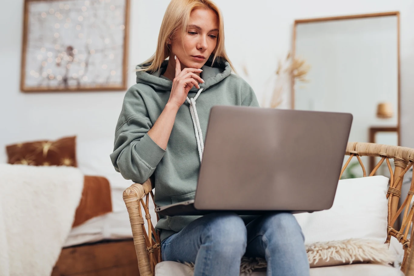 Sesje online mające na celu wzmocnienie odporności psychicznej mogą być skutecznym i dostępnym narzędziem Kobieta w zielonej bluzie z kapturem siedzi na fotelu i skupiona pracuje na laptopie, trzymając dłoń przy podbródku.