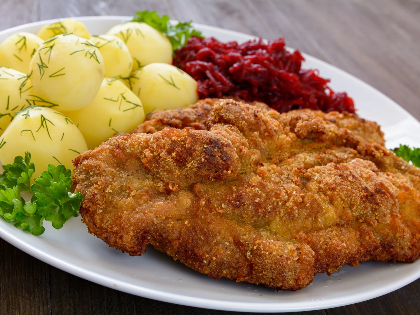 Marynata na bazie mleka sprawia, że schab po smażeniu jest kruchy i soczysty. Kotlet schabowy w panierce z ziemniakami i buraczkami, posypany koperkiem i udekorowany natką pietruszki.