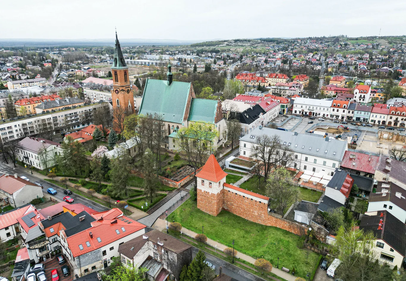 Dominująca gotycka katedra z wysoką wieżą otoczona zielenią, fragment zabytkowych murów miejskich oraz ceglana baszta w centralnej części miasta, wokół rozciąga się niska zabudowa i malownicze kamienice rynku.