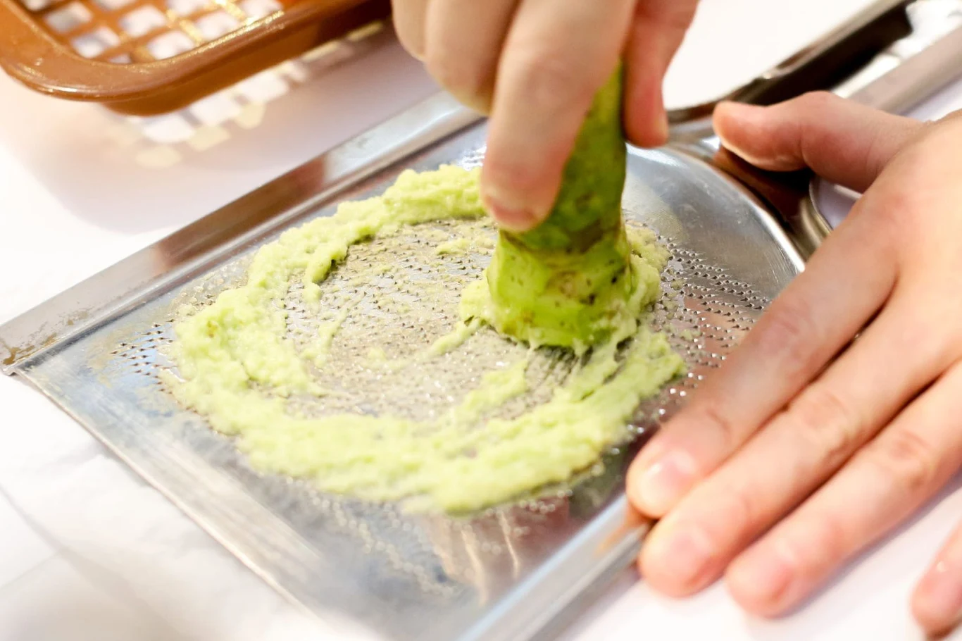 Świeży korzeń wasabi ma intensywny smak. Sprawdzi się do wielu różnych potraw Korzeń wasabi ścierany na drobnej tarce; w dłoni widoczna zielona pasta wasabi.