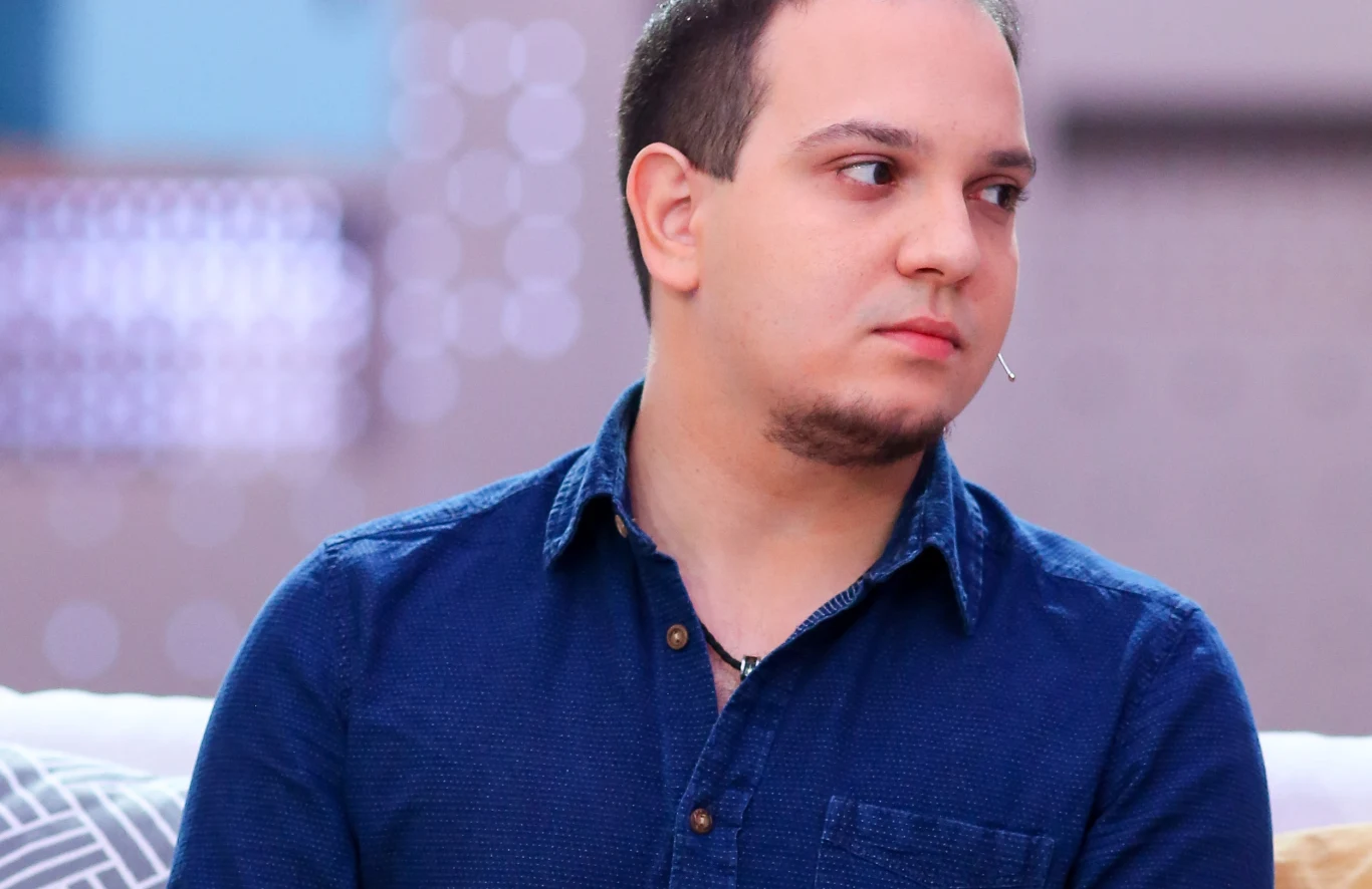 Roger Karwiński Roger Karwiński, odtwórca roli Adama w serialu Niania, w granatowej koszuli siedzi na jasnej sofie.