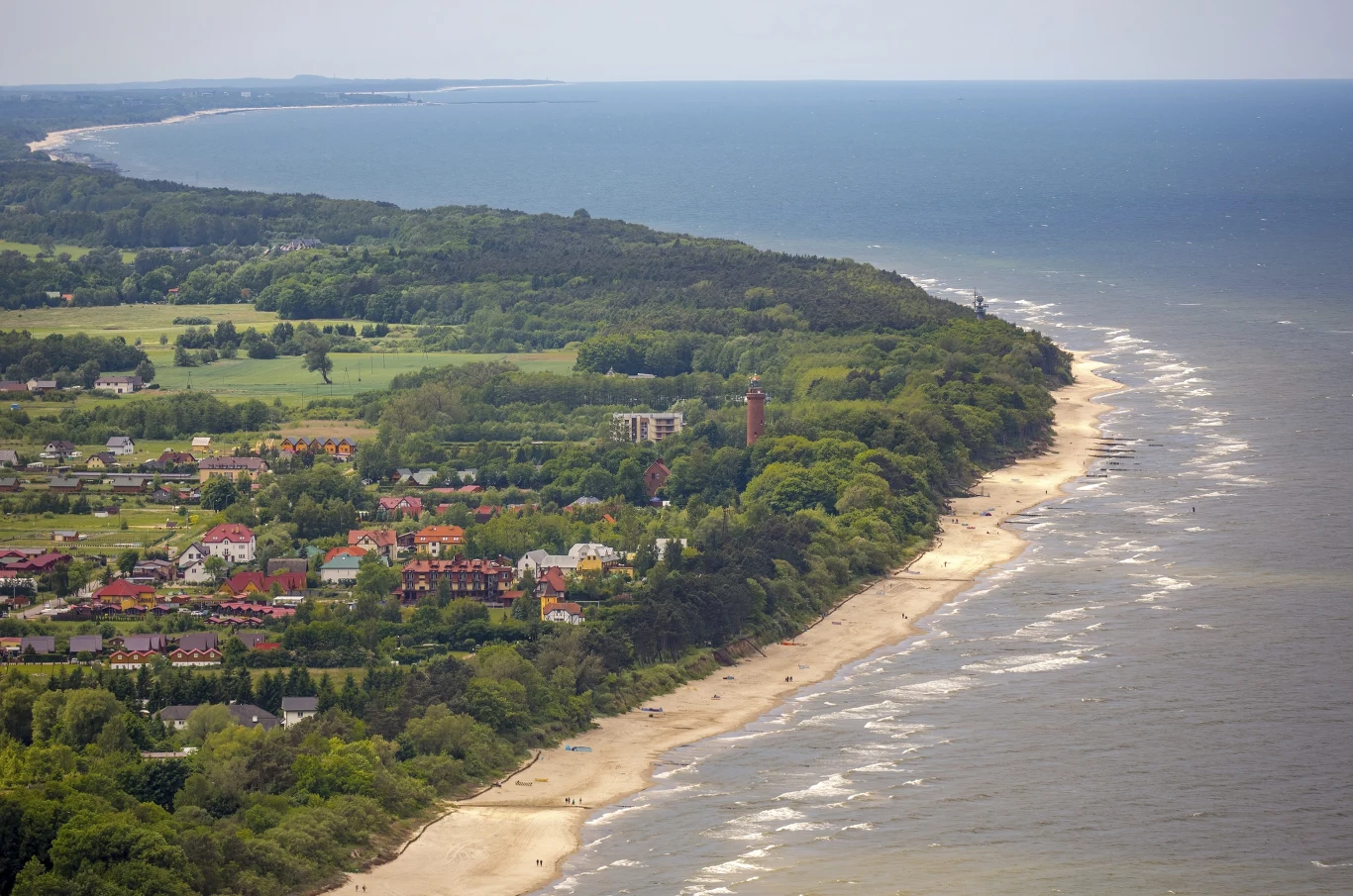Sarbinowo - wieś letniskowa niedaleko Mielna Sarbinowo, piaszczysta plaża z kilkoma osobami, spokojne morze, zabudowania przy wydmach, zachmurzone niebo
