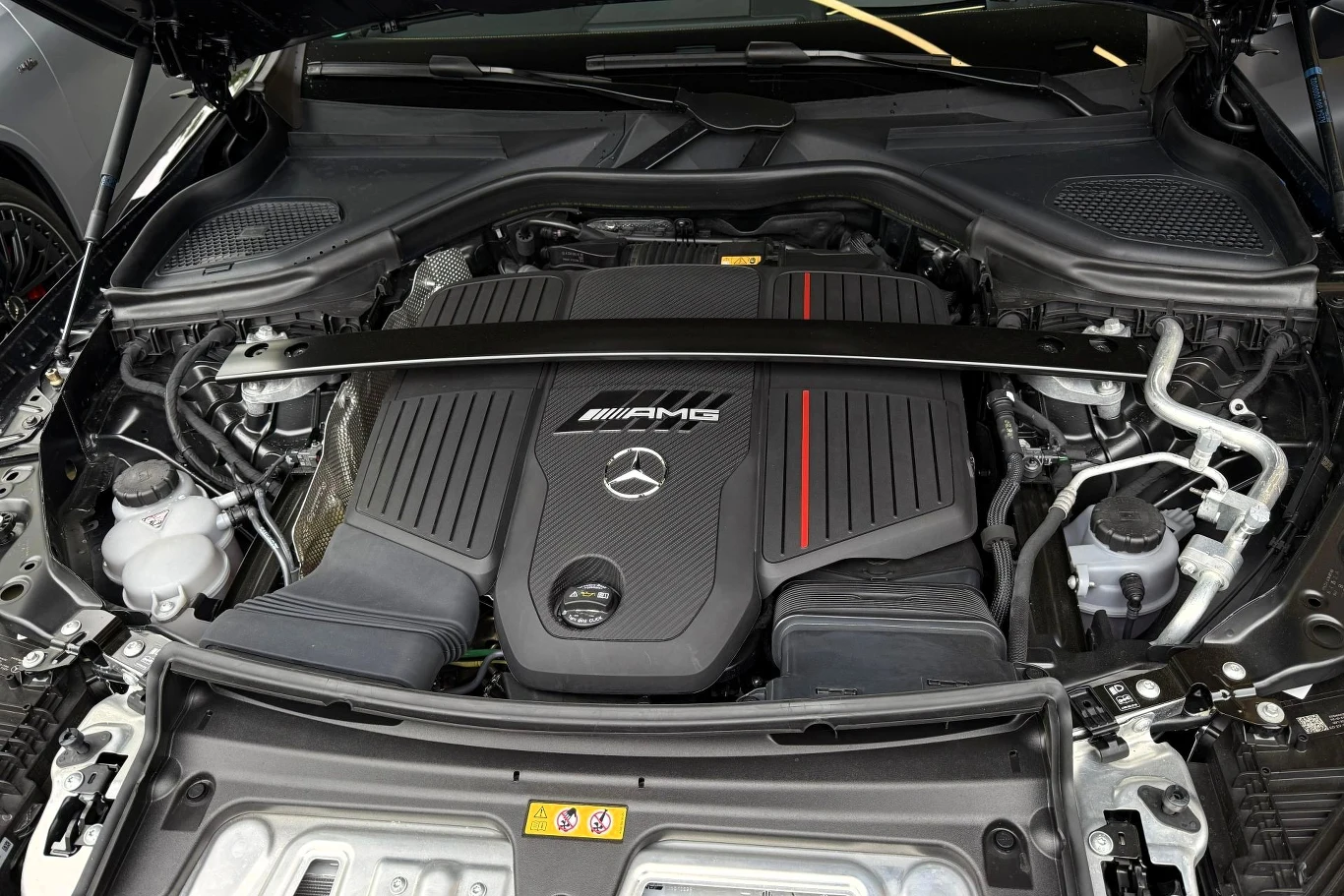 Silnik Mercedes-AMG z charakterystycznym logo i pokrywą ozdobioną czerwoną linią, otoczony elementami układu chłodzenia oraz zawieszenia.