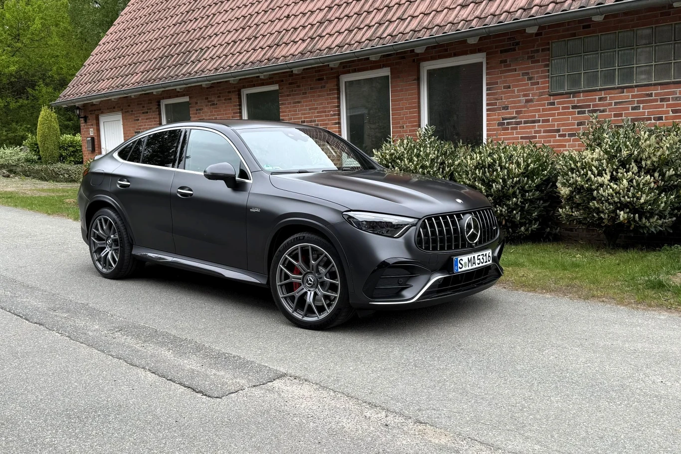 Czarny Mercedes SUV o sportowym wyglądzie stoi zaparkowany przed ceglaną zabudową z trzema białymi oknami; auto wyróżnia się dużymi felgami i charakterystycznym, błyszczącym grillem z logo marki.
