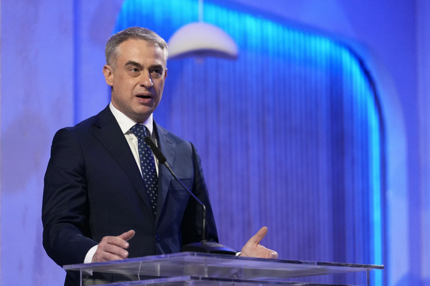 Wicepremier i minister cyfryzacji Krzysztof Gawkowski Wicepremier Krzysztof Gawkowski przemawia przy przezroczystej mównicy, w garniturze, na tle niebieskiej ściany z liniami.