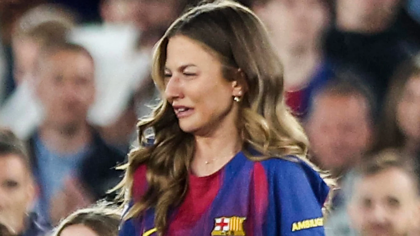 Kobieta z długimi, falowanymi włosami ubrana w koszulkę FC Barcelony, z wyrazem smutku lub wzruszenia na twarzy, otoczona przez tłum na trybunach.