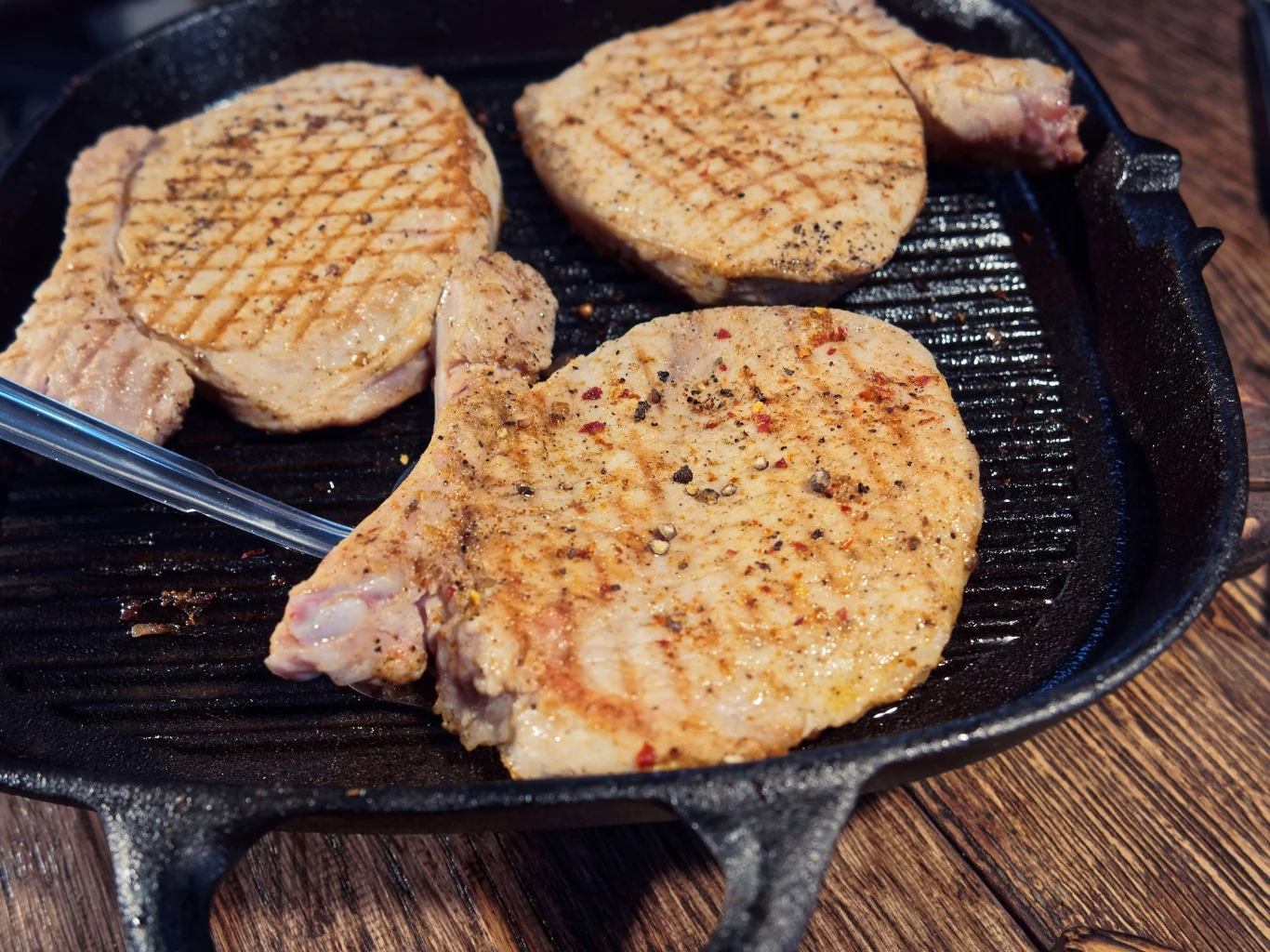 Wieprzowina złotnicka - jak ją przyrządzić? Trzy kawałki schabu ze świń złotnickich grillowane na żeliwnej patelni, z widocznymi śladami grillowania.