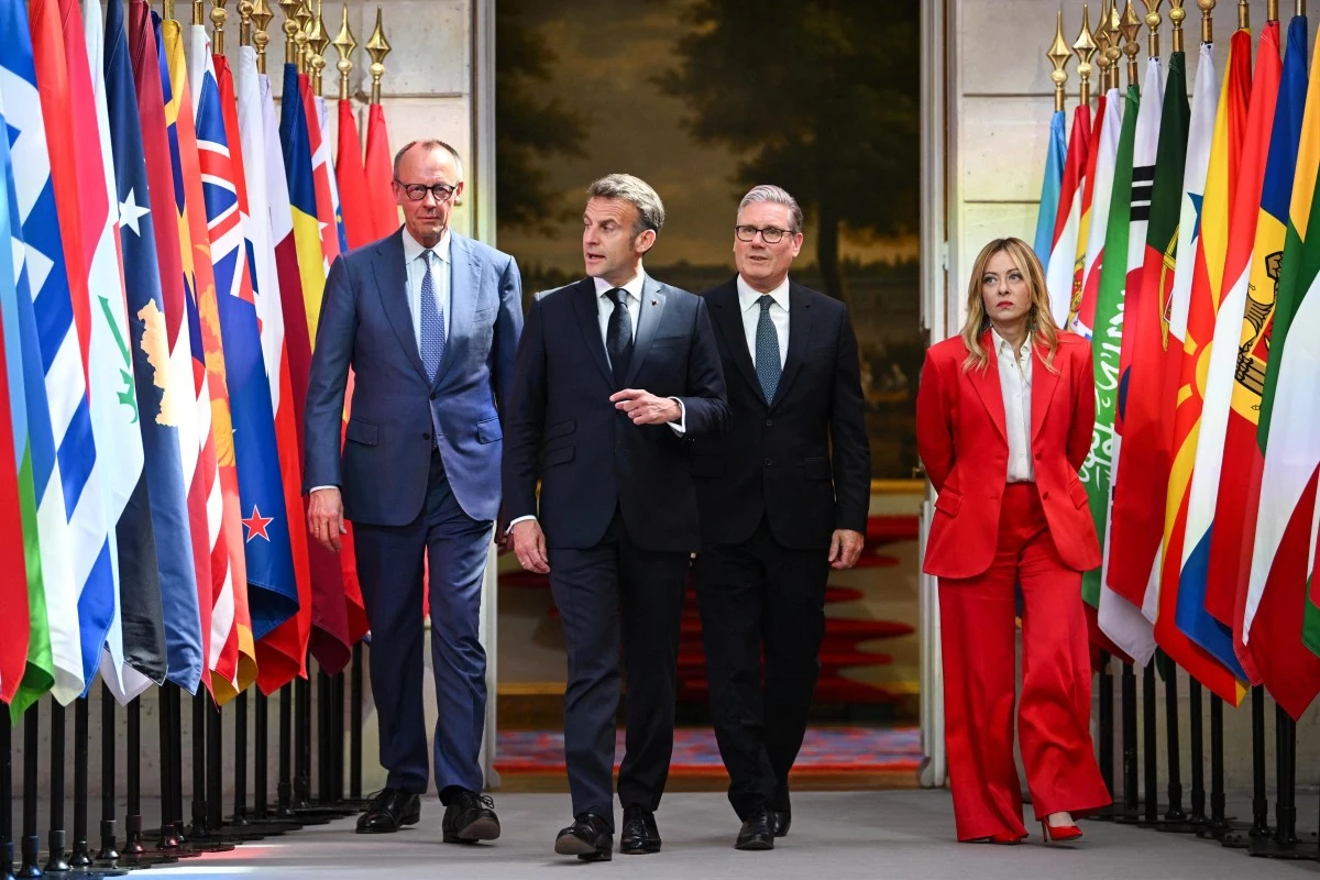 Czworo elegancko ubranych osób idzie wspólnie korytarzem pomiędzy rzędami flag państwowych.